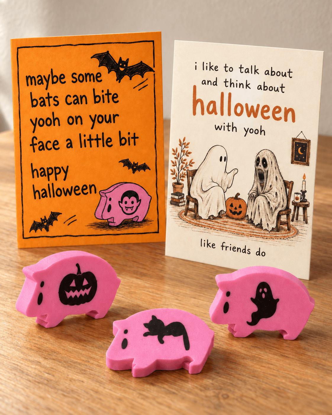 two flat halloween cards on a wooden table with pumpkin and ghost age hams standing and a cat age ham lying down